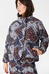 Campera capitoneada de cuello alto y manga ranglan, con diseño estampado estilo patchwork en tonos azul, bordó y blanco. Cuenta con cierre frontal con botones a presión y bolsillos laterales.