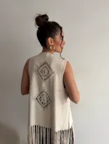Chaleco de símil gamuza color beige, sin mangas, con detalles de tejido tipo crochet y flecos largos en el ruedo.