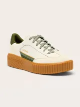 Zapatillas Sorel modelo Ona Ave T-Toe con diseño retro y plataforma. Presentan una combinación de cuero y gamuza en tonos crema, con detalles en verde oliva y suela de caucho color caramelo con textura estriada.