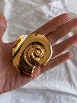 Pinza para el pelo dorada con forma de caracola.