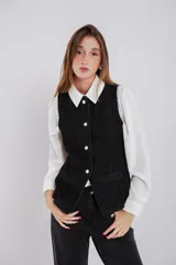 Chaleco entallado de jean negro con cuello a la base, cierre frontal con botones, bolsillos simulados y abertura en la parte trasera.