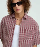 Camisa de manga corta con cuello inglés, corte oversized y estampado de cuadros en tonos rojo, blanco y negro.