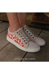 Sneakers de cuero color marfil, con diseño pintado a mano en tonos rojos y dorados en los laterales. Cuenta con suela de goma blanca, cordones beige y detalle de placa metálica con logo.