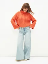 Polerón de tejido de punto color gris claro, con cuello alto y diseño de trenzas en el cuerpo y mangas. Corte holgado y puños anchos.