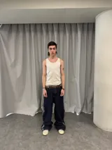 Pantalón de jean azul raw con diseño de corte versátil, ajustable mediante cierres laterales que revelan un panel interior rojo. Presenta una estampa gráfica de gran tamaño en la parte trasera con detalles bordados, costuras reforzadas y etiqueta de cuero en la cintura.