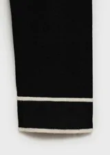 Jersey de punto fino de manga larga en color negro, con cuello en V y detalles de líneas blancas en contraste en el cuello y los puños.