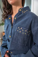 Camisa de denim negra con botones metálicos dorados y bolsillos con tachas doradas. De corte amplio.