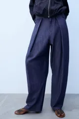 Pantalón confeccionado con lino de tiro alto con pliegues delanteros y cinco bolsillos. Presenta pernera holgada y cierre frontal con cremallera, botón interior y gancho.
