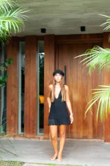 Vestido corto negro con escote en V profundo, estilo halter con tiras para atar al cuello. Presenta un diseño ajustado en el busto con tiras ajustables bajo el mismo que se cruzan y anudan en la espalda, y falda con volado en el ruedo con detalle de encaje.