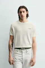 Camiseta de corte relajado, color crudo, con cuello redondo y manga corta. Presenta un pequeño estampado gráfico en el pecho con la inscripción 'Whitsunday Island'.