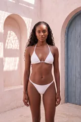 Bikini de dos piezas color blanco, con corpiño triangular con tirantes finos para atar al cuello y bombacha clásica de tiro bajo con tiras finas en los laterales.