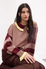 Cardigan de punto con cierre frontal de doble cursor, diseño a rayas horizontales en tonos bordó y beige. Presenta cuello estilo polo con volados en color amarillo y puños con el mismo detalle de volados.