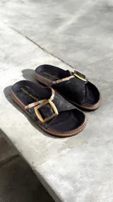 Sandalias de cuero color negro con detalles pintados a mano, tira ancha con hebilla metálica grande y suela de goma.