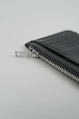 Billetera pequeña color negro con cierre de cremallera plateado y apliques de tachas metálicas redondas en la parte frontal.