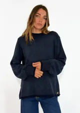 Sweater de tejido de punto en color azul marino, con cuello redondo, mangas largas con puños acanalados y ajuste holgado. Presenta un pequeño aplique decorativo en el ruedo.