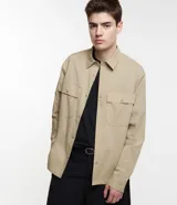 Camisa overshirt color beige, de corte recto, con cuello solapa, abotonadura frontal, mangas largas y dos bolsillos de parche con solapa en el pecho.