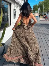 Vestido largo tipo solera, con escote en V profundo y tirantes finos. Presenta un estampado paisley en tonos rosados, lilas y blancos, con ajuste de lazo en la cintura y volados en el ruedo.