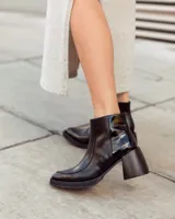 Botas de cuero negras con punta cuadrada, tacón ancho y detalles de textura en relieve en la parte superior.