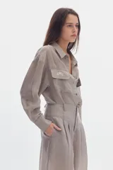 Camisa gris de efecto sedoso, manga larga, con cuello clásico, cierre frontal con botones y bolsillos delanteros con solapa y bordado.