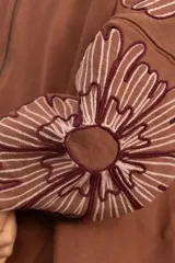 Campera bomber de jogging color marrón, con cierre frontal y bordados florales en las mangas.