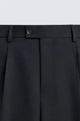Pantalón de traje negro de corte regular fit, con pinzas delanteras, bolsillos laterales y cierre frontal con cremallera y botón.