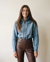 Camisa de lino celeste con cuello alto con volado y lazo, manga larga con puños abotonados y botones forrados a tono en el frente.