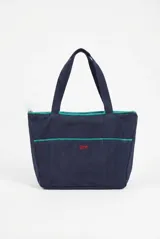 Bolso shopper de algodón en color azul marino con detalles de ribetes en color verde esmeralda. Presenta doble asa de hombro, cierre superior y bolsillos frontales con el logo bordado en color rojo.