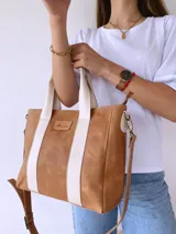 Bolso tipo tote de cuero color camel con dos tiras verticales blancas y correa larga ajustable al hombro.