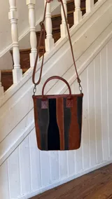 Matera de cuero con diseño de paneles verticales en combinación de colores azul, verde, marrón y bordó. Cuenta con dos asas cortas de cuero y estructura rígida.