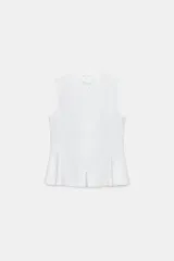 Camisa sin mangas de color blanco, con cuello subido y cierre frontal mediante nudos de pasamanería china. Presenta diseño entallado con bajo en peplum.