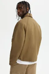 Campera de sarga levemente acolchada con cuello inglés, cierre frontal y solapa con botones. Presenta mangas raglán, bolsillos insertados delanteros y cordón ajustable en el bajo.