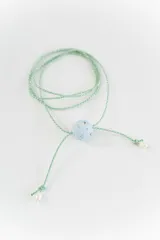 Gargantilla tipo bolo tie de tiento trenzado verde con dije esférico celeste con brillos incrustados.