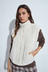 Chaleco de corderito color marrón oscuro, con cierre frontal completo, cuello alto y bolsillos laterales.