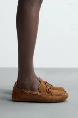 Mocasín casual de cuero color marrón claro con acabado serraje, horma redonda, detalle de lazo en el empeine y suela de goma.