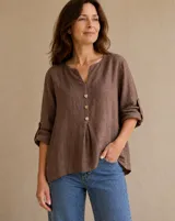 Blusa de lino color marrón chocolate, de corte holgado, con escote en V y tres botones frontales. Las mangas son largas con trabilla para sujetarlas dobladas.