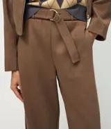 Pantalón de corte barrel, color marrón, confeccionado en algodón con felpa. Presenta cintura alta con cinto aplicado y hebilla metálica, y piernas de diseño amplio y cónico hacia los tobillos.