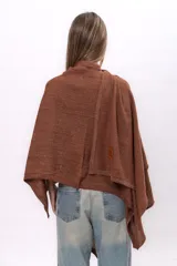 Ruana tejida de punto con cuello alto, confeccionada en una mezcla de algodón y lurex que le otorga un acabado brillante. Presenta un diseño asimétrico con caída fluida y holgada.