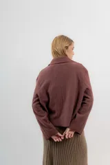 Chaqueta corta tipo blazer color marrón, confeccionada en tela de lana afieltrada. Tiene cuello camisero, silueta cuadrada, cierre frontal con botones y bolsillos delanteros.