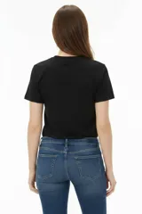 Remera de algodón negra de manga corta y cuello redondo, con estampa frontal que incluye letras rojas y gráficos en tonos dorados.