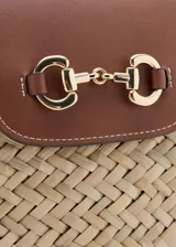 Bolso de mano y hombro de fibra natural trenzada tipo paja, con detalles de cuero sintético marrón, doble asa de hombro, solapa frontal con cierre metálico dorado y forro interior de tela.