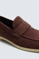 Mocasín casual de hombre, color marrón oscuro (bordó), fabricado en piel con acabado serraje (gamuza). Presenta un detalle de antifaz en el empeine y suela a contraste de color beige claro.