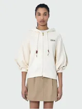 Canguro color crema con capucha, cierre frontal con cremallera dorada, mangas abullonadas 3/4 y logo de la marca en el pecho.