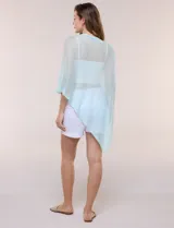 Poncho liviano de tejido de punto fino calado, color blanco, con silueta asimétrica envolvente, escote bote drapeado y mangas integradas estilo capa.