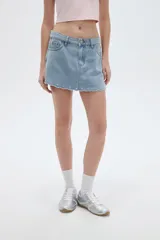 Short pollera de denim celeste claro, de tiro alto y corte mini, con diseño de falda cruzada al frente y detalle de ojales metálicos decorativos en el ruedo.