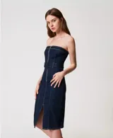 Vestido midi de jean azul oscuro, corte recto, sin mangas y con escote recto. Presenta cierre frontal con cremallera metálica, cinturón con hebilla forrada y abertura en el centro.
