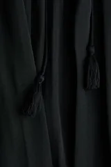 Pollera maxi negra de corte holgado, confeccionada con cintura elástica fruncida y cordón ajustable con borlas colgantes.