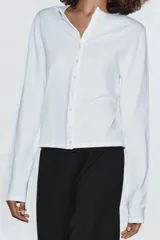 Camiseta de manga larga confeccionada en algodón 100%, con cuello redondo y cierre frontal mediante una hilera de botones pequeños.