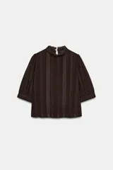 Camisa marrón oscuro de cuello subido y manga corta abullonada, con detalles de puntilla a tono y cierre posterior con botón.