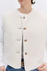 Chaleco reversible de diseño acolchado con costuras en rombos, color tostado con interior de corderito blanco. Presenta cierre frontal con botones, cuello redondo y bolsillos delanteros.