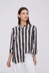 Camisa de manga larga con cuello clásico y cierre frontal de botones. Presenta un estampado de rayas verticales irregulares en tonos oscuros, blancos y verde claro.